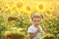 A little girl in a field with tall sunflowers at sunset is gnawing on sunglasses with a happy, thoughtful look. Royalty Free Stock Photo