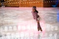 Little girl figure skater in a pink sweater is skating on winter evening on an outdoor ice rink lit by garlands Royalty Free Stock Photo