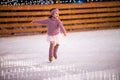 Little girl figure skater in a pink sweater is skating on winter evening on an outdoor ice rink lit by garlands Royalty Free Stock Photo