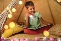 Little girl with flashlight reading book in tent Royalty Free Stock Photo