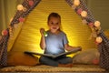 Little girl with flashlight reading book in play tent Royalty Free Stock Photo