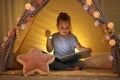 Little girl with flashlight reading book in play tent Royalty Free Stock Photo