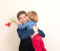 Little girl with flowers kissing her elder brother. Teen boy congratulates his little sister and gives her flowers tulips