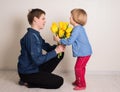 Little girl with flowers kissing her elder brother. Teen boy congratulates his little sister and gives her flowers tulips Royalty Free Stock Photo