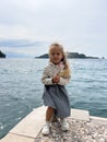 Little girl with flying hair sits on a bollard on a pier by the sea