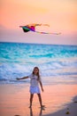 Little girl with flying kite on tropical beach at sunset. Kid play on ocean shore with beach toys. Royalty Free Stock Photo