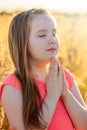 Little girl folded her hand and close your eyes in praying, dreaming in field outdoors. Child praying Royalty Free Stock Photo