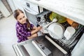 Little girl folding dishes in the dishwasher in the kitchen