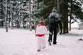 Little girl follows her mother through snowdrifts in a snowy forest. Back view