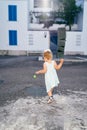Little girl follows a rolling ball on the asphalt near the house