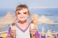 Little girl without front teeth, holds chocolate ice cream cone in hand. Cheerful child with two ice cream on the beach. Babe in