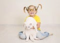 Little girl in funny bee glasses and yellow t-shirt and with braids smiling happy hugging her cat Royalty Free Stock Photo