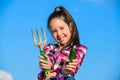 Little girl gardener work at family farm. Kid cheerful gardener holds rake and cucumber blue sky background. Girl