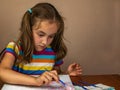 A little girl girl sitting at the table enthusiastically draws with a brush and watercolor paints on a white canvas of Royalty Free Stock Photo