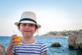 A little girl with a glass of orange juice stands on a rocky sea coast. Portrait of a child at a beach resort Royalty Free Stock Photo