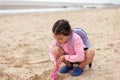 A little girl in glasses and with a backpack plays on a sandy beach in clothes. Bad weather on summer holidays at sea Royalty Free Stock Photo