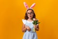 Little girl in glasses and easter bunny ears on a yellow background. The child is holding a bouquet of tulips. Waist up close up Royalty Free Stock Photo