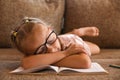A little girl with glasses fell asleep on the couch reading a book while studying at home Royalty Free Stock Photo