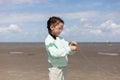 A little girl in glasses is winding her wind kite while standing on a sandy beach