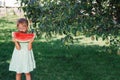 Little girl in green dress, barefoot standing in the park with big slice watermelon. Royalty Free Stock Photo