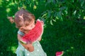 Little girl in green dress, barefoot standing in the park with big slice watermelon. Royalty Free Stock Photo