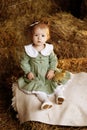 A little girl in a green dress sits in a rural barn on the hay with a duckling. Royalty Free Stock Photo