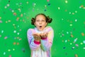 A little girl on a green isolated background in a bright suit blows away a streamer. Space for text. The concept of a holiday,