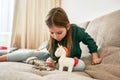 A little girl in a green pullover is sitting alone on a sofa examining coins having her unicorn moneybox around sdgsdfg