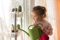 A little girl with a green watering can is playing on the window of the house and watering the flowers. Royalty Free Stock Photo