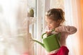 A little girl with a green watering can is playing on the window of the house and watering the flowers. Royalty Free Stock Photo