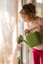 A little girl with a green watering can is playing on the window of the house and watering the flowers. Royalty Free Stock Photo