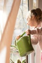 A little girl with a green watering can is playing on the window of the house and watering the flowers. Royalty Free Stock Photo