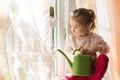 A little girl with a green watering can is playing on the window of the house and watering the flowers. Royalty Free Stock Photo