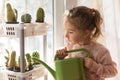 A little girl with a green watering can is playing on the window of the house and watering the flowers. Royalty Free Stock Photo