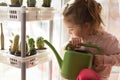 A little girl with a green watering can is playing on the window of the house and watering the flowers. Royalty Free Stock Photo