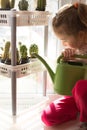 A little girl with a green watering can is playing on the window of the house and watering the flowers. Royalty Free Stock Photo