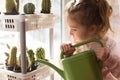 A little girl with a green watering can is playing on the window of the house and watering the flowers. Royalty Free Stock Photo