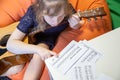A little girl learns to play the guitar by sheet music