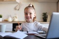 Little girl handwrite study online using laptop at home, cute happy small child take Internet web lesson or class on PC