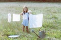 Little girl hangs out to dry retro doll clothes, summer nature outdoor. Washing, children`s games, kid`s leisure