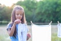 Little girl hangs out to dry retro doll clothes, summer nature outdoor. Washing, children`s games, kid`s leisure