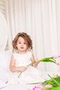 Little girl with a happy smile. Holds flowers. Dressed in a white dress and white socks.