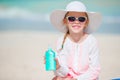 Little girl in hat with bottle of sun cream sitting at sunbed on tropical beach Royalty Free Stock Photo