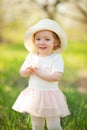 Little girl in a hat is cheerful, in a blooming garden or park. Warmly, love, spring and summer mood Royalty Free Stock Photo