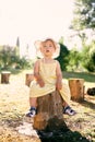 Little girl in a hat and dress sits on a tree stump in the park Royalty Free Stock Photo