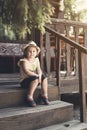 Little girl in a hat sits on the porch of an old wooden house Royalty Free Stock Photo