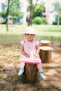 Little girl in a hat sits on a tree stump in the yard Royalty Free Stock Photo