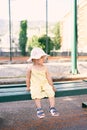 Little girl in a hat sits on a wooden bench near the fence of the park Royalty Free Stock Photo