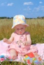 Little girl in a hat sitting on green field Royalty Free Stock Photo