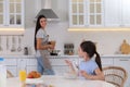 Little girl having breakfast while mother cooking food in kitchen. Single parenting Royalty Free Stock Photo